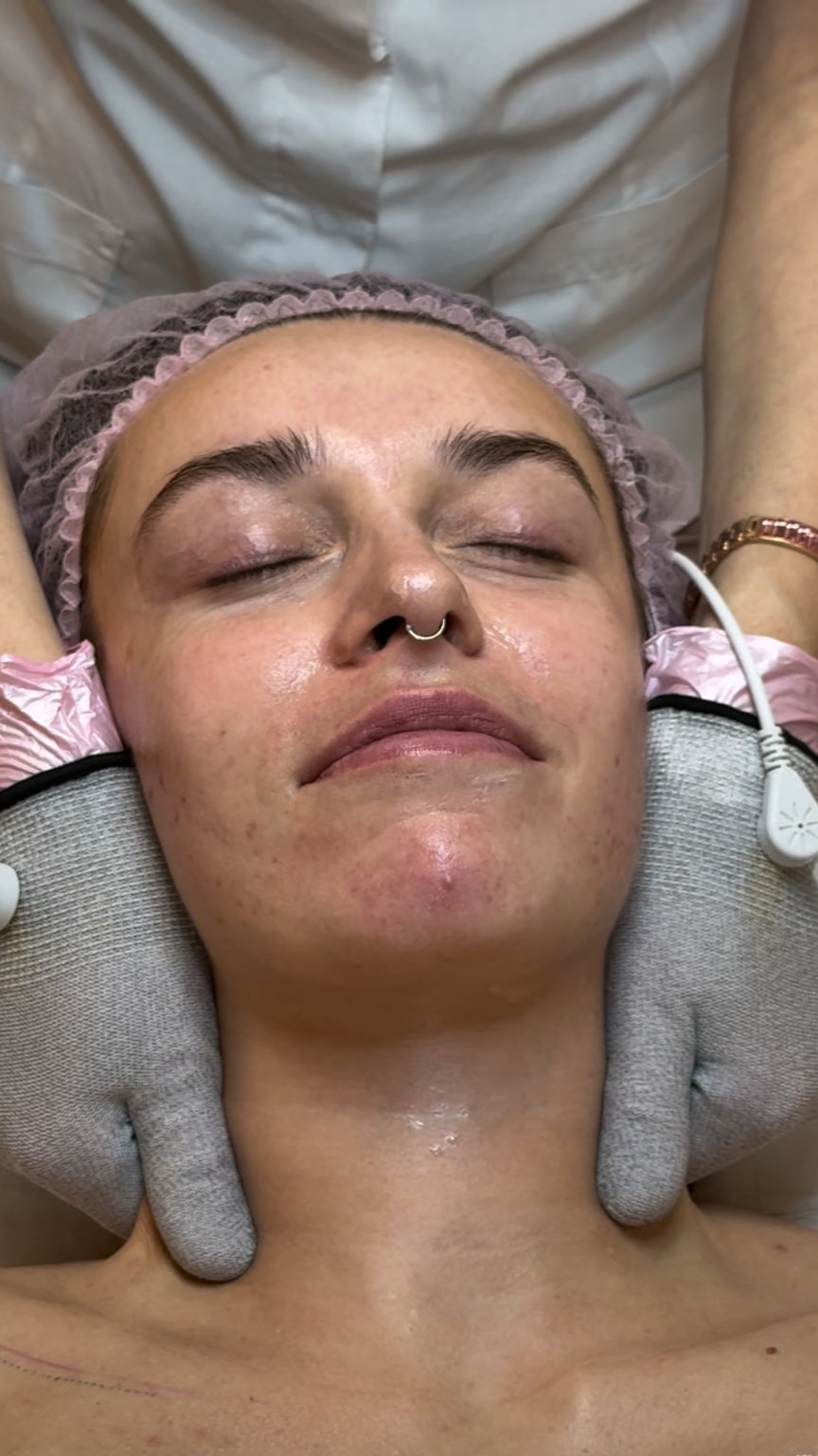 Mikrostrom-Behandlung des Gesichts mit grauen Handschuhen und rosa Überschuhen